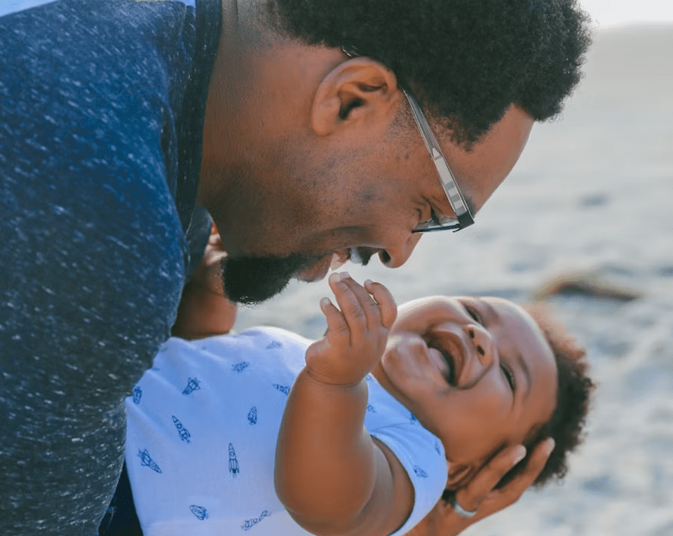 A young father and his child smiling and laughing at one another.